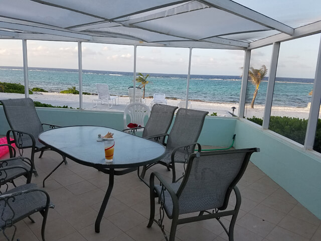 Screened seaside porch with an outdoor table overlooking the ocean